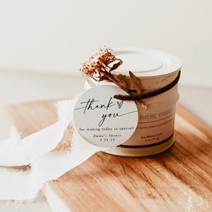 May include: A white candle jar with a brown ribbon and a white tag that says "Thank you for making today so special! Emma's Shower 9.24.25". The candle jar is labeled "Cashmere Vanilla Soy Blend Candle 6 oz (171 g)".