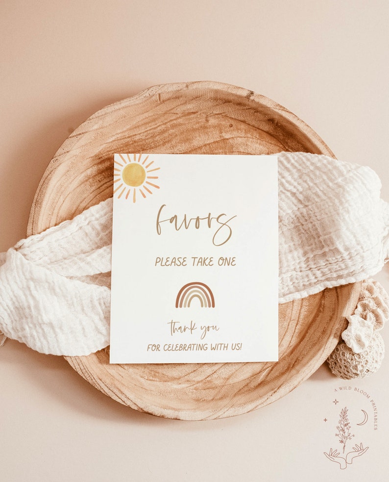 May include: A white card with the word "favors" written in brown cursive script. The card has a sun and rainbow graphic and the text "Please take one", "Thank you", and "For celebrating with us!"