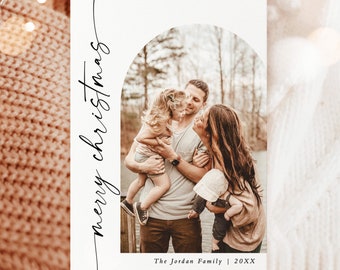 May include: A Christmas card with a family photo inside an arch. The words "merry christmas" are written in a script font on the left side. The family is standing near a body of water. The text "The Jordan Family | 20XX" is at the bottom.