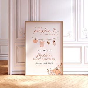 May include: A rectangular poster in a thin frame featuring the text A LITTLE PUMPKIN IS ON HER WAY, WELCOME TO Maddie's BABY SHOWER, and October 22nd, 20XX. The design includes a clothesline with a pumpkin, onesie, shoes, and flowers.