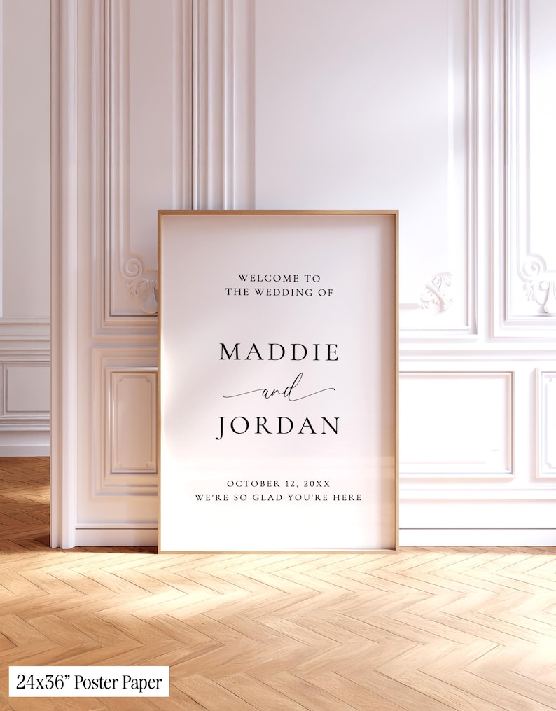 May include: A 24x36 inch wedding welcome sign in a thin wooden frame. The white poster features black text reading: WELCOME TO THE WEDDING OF MADDIE and JORDAN OCTOBER 12, 20XX WE'RE SO GLAD YOU'RE HERE. The design uses a mix of serif and script fonts.