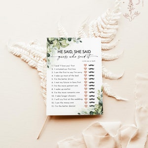 May include: A white card with the text "He Said, She Said guess who said it" surrounded by green foliage. The card has a list of statements with mustache and heart icons for circling. A Wild Bloom Printables logo is in the top right.