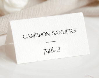 Op de afbeelding: Witte plaatskaart met zwarte tekst "Cameron Sanders" en "Tafel 3".