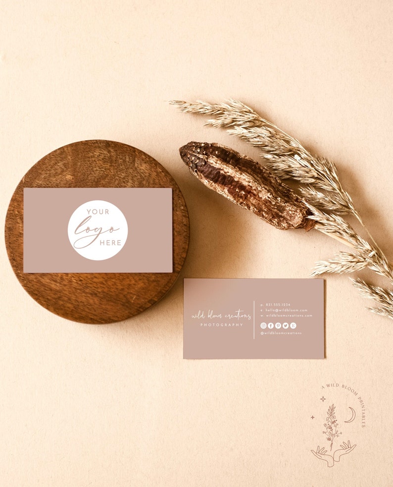 May include: A light brown business card with the text "wild bloom creators photography" and contact information. The card is on a beige background with a dried grass stalk and a wooden coaster with a second business card that says "YOUR LOGO HERE" in a circle.