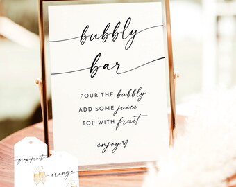 May include: A printable sign for a bubbly bar with the text "bubbly bar", "pour the bubbly", "add some juice", "top with fruit", and "enjoy". The sign is in a gold frame and there are two tags with the text "grapefruit" and "orange" with illustrations of champagne glasses.
