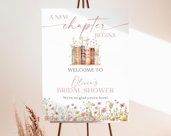 May include: A white 18x24 inch foam board sign on a metal easel. The text reads A NEW chapter BEGINS, WELCOME TO Olivia's BRIDAL SHOWER, We're so glad you're here! It features a watercolor illustration of books and colorful wildflowers.