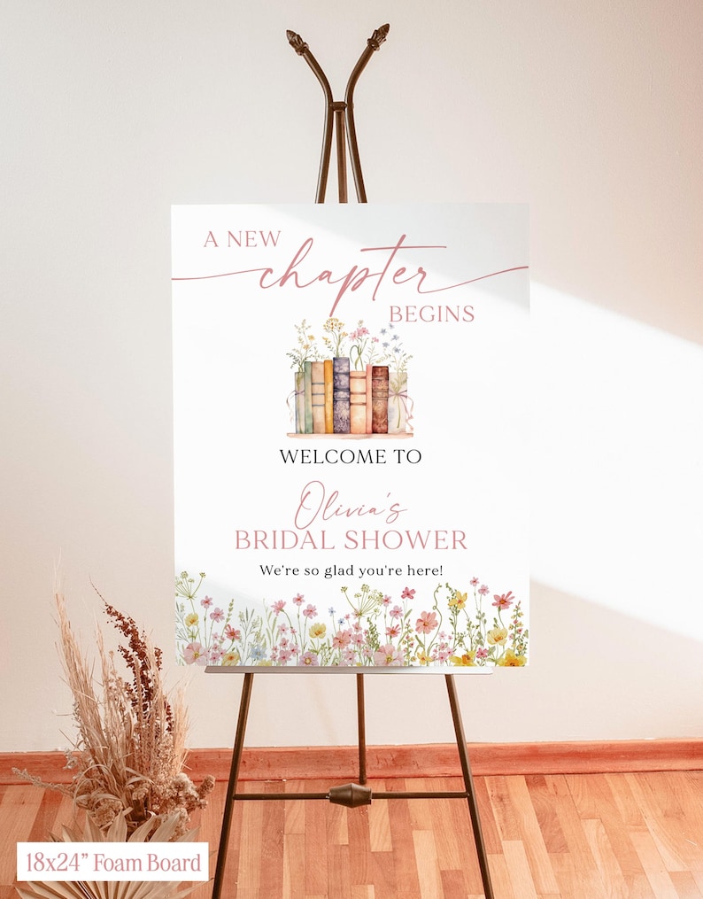 May include: A white foam board sign on a brown easel. The sign reads "A New Chapter Begins" and "Welcome to Olivia's Bridal Shower." Floral illustrations and text are in pink and brown. The sign is 18x24 inches.