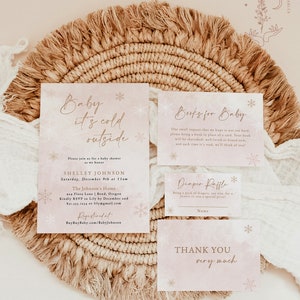 Op de afbeelding: Een setje baby shower briefpapier met een aquareleffect. De uitnodiging luidt "Baby it's cold outside" met sneeuwvlokdetails. Inclusief kaarten voor boeken, een luier verloting en bedankjes. Het ontwerp is in zachtroze en goud.