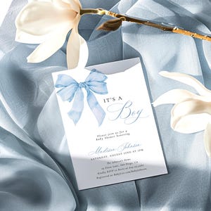 May include: A baby shower invitation with a blue bow and the text "It's a Boy" in a cursive font. The invitation includes the date, time, and location of the shower, as well as the name of the guest of honor, Madison Johnson.