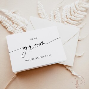 Op de afbeelding: Een witte kaart met zwarte tekst die "To my groom on our wedding day" zegt.