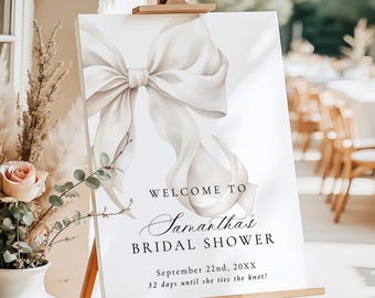May include: A white sign on a wooden easel featuring a large bow illustration. The sign says "WELCOME TO Samantha's BRIDAL SHOWER" with the date and a countdown. The sign is displayed outdoors, indicating a wedding or bridal event.