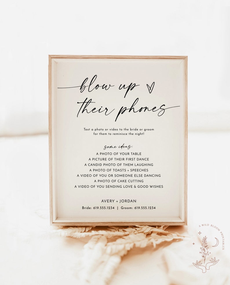 May include: A white sign with a wooden frame, with the text "blow up their phones" in black cursive font. The sign also includes instructions to text a photo or video to the bride and groom, along with some ideas for what to send. The sign includes the names Avery and Jordan, and their phone numbers.