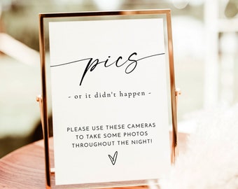 Puede incluir: Un cartel con marco dorado con el texto "pics - or it didn't happen -" y un mensaje que anima a los invitados a usar las cámaras proporcionadas para tomar fotos durante toda la noche. El cartel está sobre una mesa de madera con un diseño floral en la parte inferior.