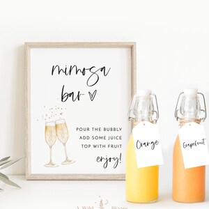 May include: A printable sign that says "mimosa bar" with a heart symbol. The sign is framed in a light wood frame. There are two glass bottles with orange juice, one labeled "Orange" and the other labeled "Grapefruit".