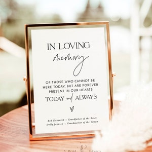 May include: A white sign in a gold frame with the text "In loving memory" and a handwritten script of "memory". The sign also includes the text "Of those who cannot be here today, but are forever present in our hearts today and always". The sign also includes the names "Bob Denewith" and "Dolly Johnson" with their respective titles "Grandfather of the Bride" and "Grandmother of the Groom".