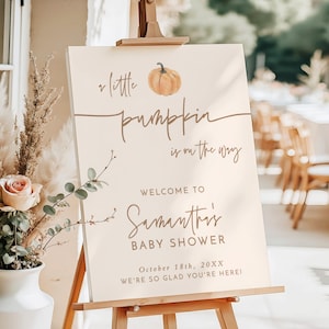 May include: A rectangular 18x24 inch foam board sign on a wooden easel. The sign is cream-colored with brown text reading: A little pumpkin is on the way, WELCOME TO Samantha's BABY SHOWER, October 18th, 20XX, WE'RE SO GLAD YOU'RE HERE!