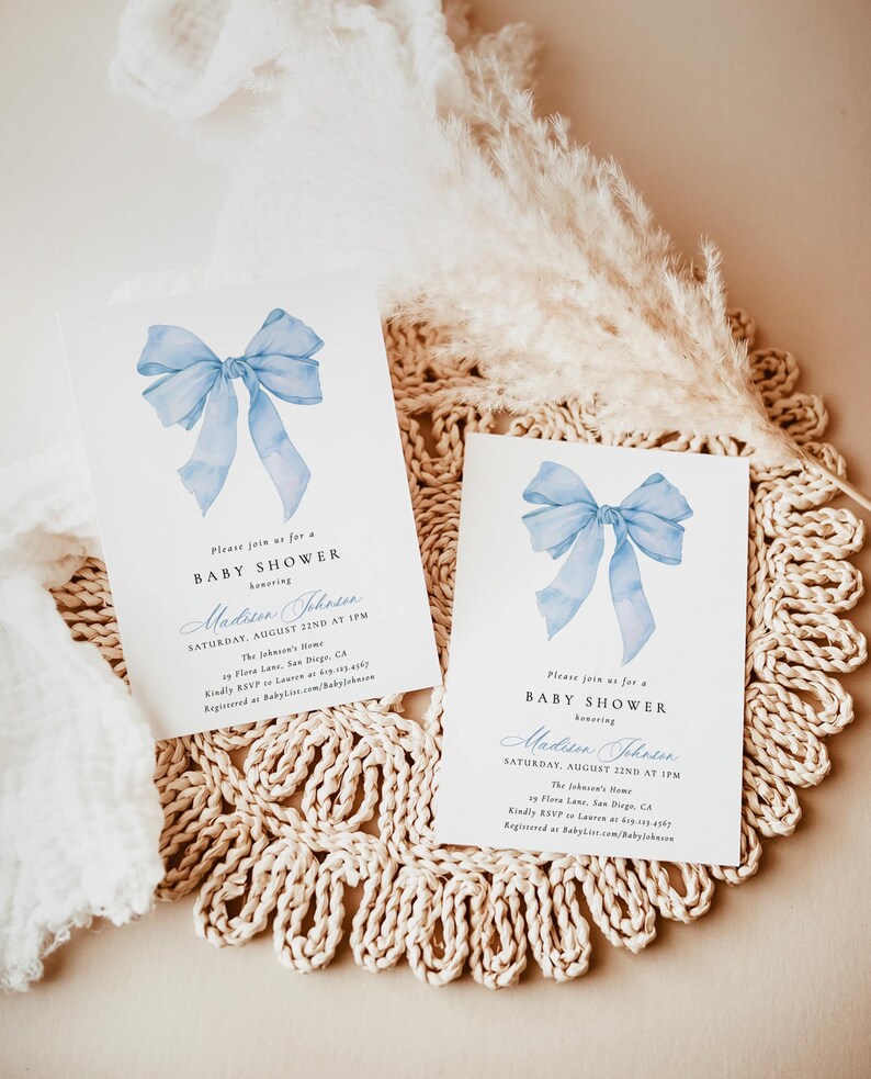 Może przedstawiać: Dwa zaproszenia na baby shower z akwarelowym wzorem niebieskiej kokardy. Tekst brzmi "Please join us for a BABY SHOWER honoring Madison Johnson, Saturday, August 22nd at 1PM". Zaproszenia leżą na beżowej, tkanej podkładce.