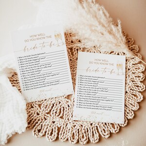 May include: Two printable game cards with a gold glitter background and a watercolor illustration of champagne flutes. The cards are titled "How Well Do You Know The Bride-To-Be?" and feature a list of questions about the bride.