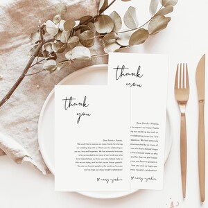May include: Two white thank you cards with black calligraphy text. The text reads "thank you" and includes a message expressing gratitude to family and friends for attending the wedding. The cards are on a white plate with a gold fork and knife.