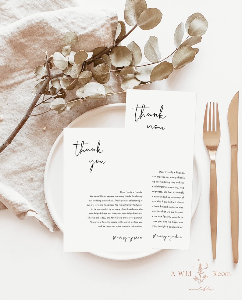 May include: Two white thank you cards with black calligraphy text. The text reads "thank you" and includes a message expressing gratitude to family and friends for attending the wedding. The cards are on a white plate with a gold fork and knife.