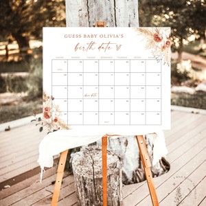 Puede incluir: Un calendario imprimible blanco con un dise&ntilde;o floral y el texto "Adivina la fecha de nacimiento de la beb&eacute; Olivia" en texto marr&oacute;n. El calendario es para junio y julio y tiene una fecha de vencimiento marcada el 17 de junio.