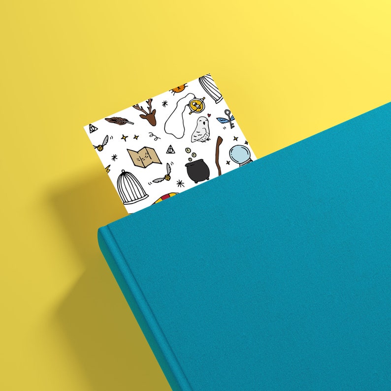 K&ouml;nnte beinhalten: Ein wei&szlig;es Lesezeichen mit einem blauen Buch. Das Lesezeichen zeigt ein Muster aus verschiedenen Harry-Potter-Motiven, darunter eine Eule, ein K&auml;fig, ein Zauberstab, eine Karte und ein Kessel.