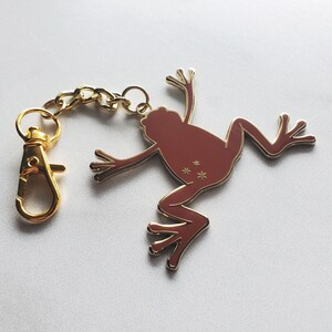 May include: A gold-tone keychain featuring a red frog with gold accents. The frog has a detailed design with stars on its back.