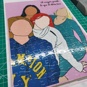 May include: A completed jigsaw puzzle featuring a group of four stylized figures. The figures have different skin tones and hair colors. The puzzle is set against a pink background with text in Spanish. The figures are wearing various tops.
