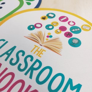 May include: A white circular classroom-themed design with the text "THE CLASSROOM BOOK" in teal and pink. The design includes an open book illustration and various school-related icons in a yellow and pink color scheme.