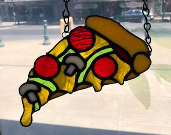 May include: A stained glass pizza slice hanging from a chain. The pizza is yellow with green, red, and white toppings.