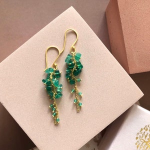 Peut inclure: Boucles d'oreilles pendantes dorées avec une cascade de perles de pierres précieuses vertes.