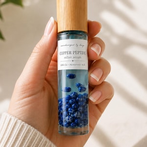 May include: A clear glass roller serum bottle with a light wood cap. The label reads neurodivergent by design COPPER PEPTIDE roller serum GHK-Cu Hyaluronic Acid. The bottle contains a clear liquid and numerous small, round, blue speckled beads.