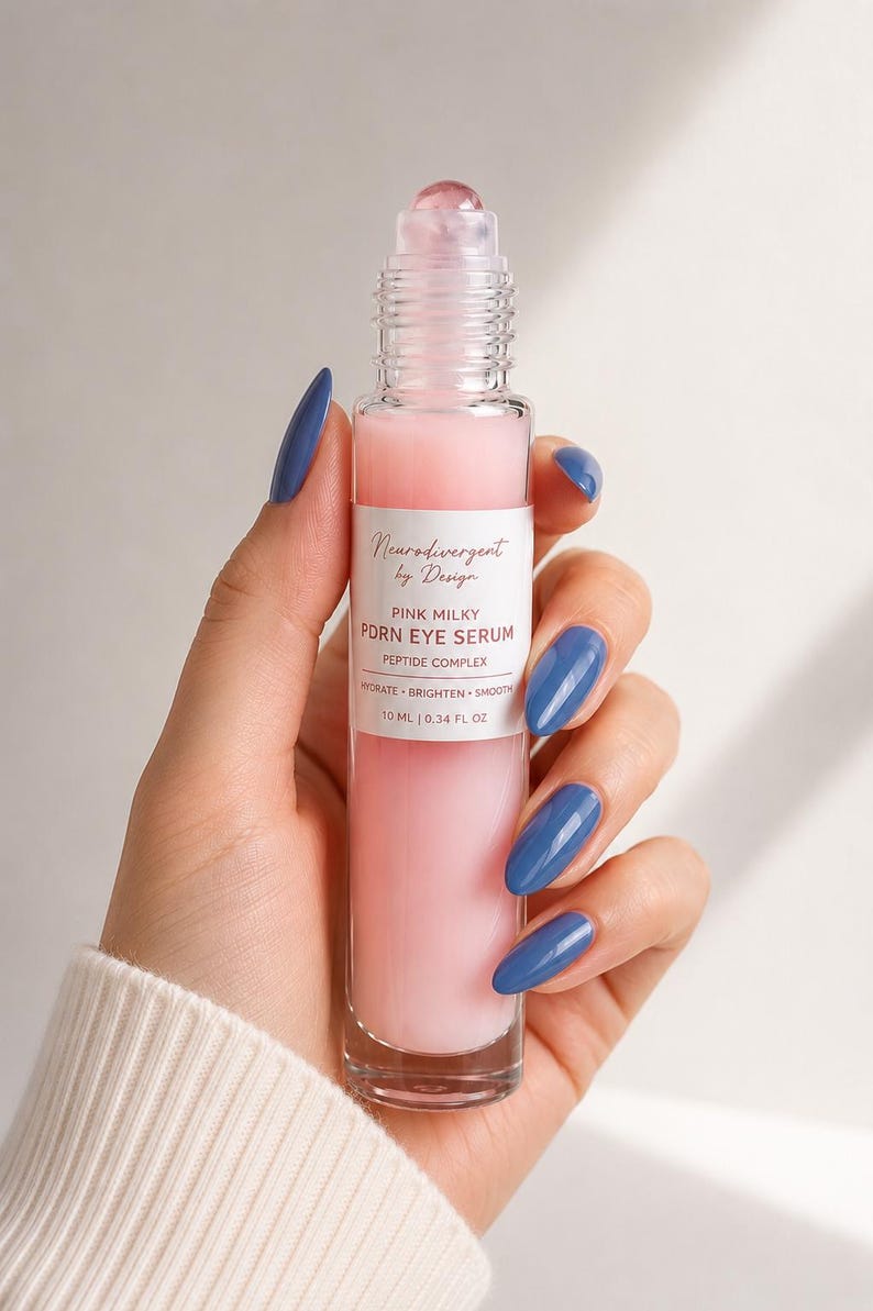 Peut inclure: Un flacon &agrave; bille en verre transparent contenant un s&eacute;rum pour les yeux rose laiteux. L'&eacute;tiquette blanche indique Neurodivergent by Design, PINK MILKY PDRN EYE SERUM, PEPTIDE COMPLEX, HYDRATE BRIGHTEN SMOOTH, et 10 ml | 0.34 fl oz. Bouchon transparent.