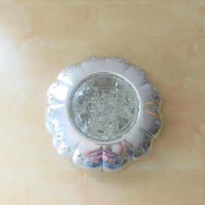 May include: Silver-plated flower vase with a glass insert and a scalloped edge. The vase has a decorative design of leaves and flowers.