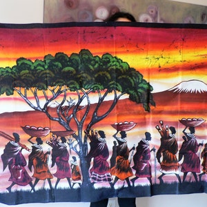 Puede incluir: Un tapiz de pared de batik colorido que representa una escena de personas caminando por un paisaje de sabana. La escena presenta un &aacute;rbol grande, una monta&ntilde;a en la distancia y un cielo de puesta de sol. Las personas llevan cestas y otros art&iacute;culos en sus cabezas.