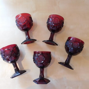 May include: Set of five red glass goblets with a textured design. The goblets have a square base and a round bowl.