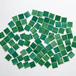 May include: A collection of small, square, green ceramic tiles. The tiles are arranged in a random pattern and are scattered across a white background.