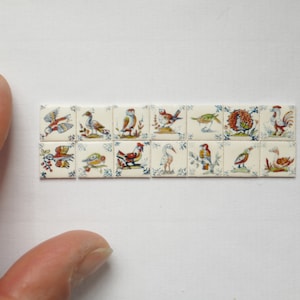 May include: A set of 16 small, square ceramic tiles with hand-painted images of birds. The tiles are white with blue and red accents. The birds are depicted in various poses, some flying, some perched, and some standing.