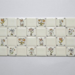 Könnte beinhalten: Eine weiße Fliesenwand mit einem Muster aus 16 kleinen quadratischen Fliesen, jede mit einem anderen floralen Design in Gelb-, Orange-, Grün- und Blautönen.