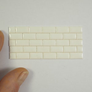 Può includere: Un piccolo foglio di piastrelle in ceramica bianca, ogni piastrella ha un bordo leggermente rialzato. Le piastrelle sono disposte a forma di mattone.