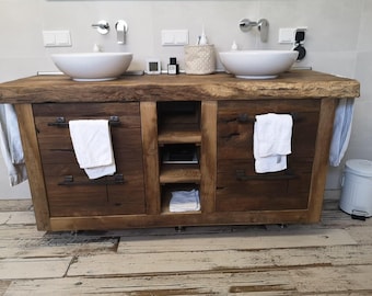May include: A rustic wooden bathroom vanity featuring a live-edge countertop, two white ceramic vessel sinks, and two cabinets with dark metal hardware. Each cabinet door holds a white towel. The center section includes three open storage shelves.