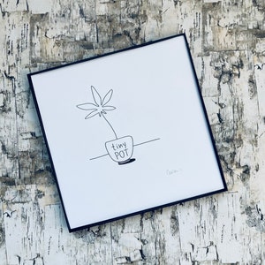 May include: A black and white line drawing of a plant in a pot with the text "tiny pot" written on the pot. The drawing is framed in a black frame.