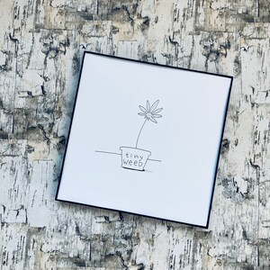 May include: A black framed print featuring a minimalist line drawing of a cannabis plant in a pot. The pot is labeled "tiny weed" in a handwritten font. The artwork is on a white background.