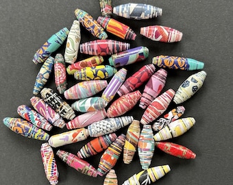 May include: A collection of colorful, paper-wrapped beads in various patterns and colors, including red, yellow, blue, and green. The beads are oval-shaped and appear to be handmade, perfect for jewelry making or craft projects.
