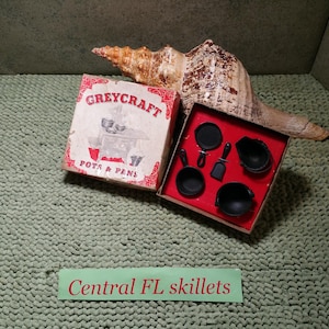 May include: A Greycraft Pots & Pans miniature set in a box with red and white graphics, featuring small black cookware pieces including skillets and a spatula, displayed with a large tan seashell and a sign reading Central FL skillets.