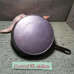 May include: A dark gray cast iron skillet with a handle, marked with "SIDNEY HOLLOWARE CO." and the number "9". The skillet is on a textured green surface. The text "Central FL skillets" is at the bottom.