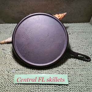 May include: A dark, round cast iron skillet with a handle, featuring the text "Wagner Ware Sidney -0-" and "PAT. DIEP FRYER". The skillet is on a textured surface with a label that reads "Central FL skillets".