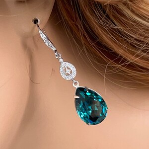 May include: Elegant silver-toned drop earring featuring a large, faceted teal teardrop-shaped gemstone. The earring has a delicate design with small, sparkling clear stones and a decorative circular element.
