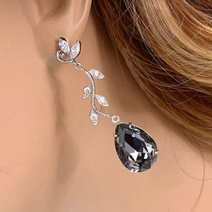 May include: Silver dangle earrings with a black teardrop-shaped crystal and a delicate leaf design.
