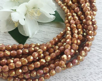 May include: A strand of iridescent copper-colored faceted glass beads. The beads are small and round, with a slightly irregular shape. The beads are strung on a clear thread and are arranged in a circular pattern.